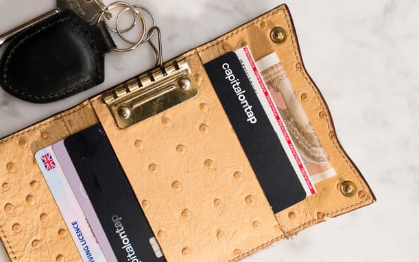 Open Tan Textured Wallet With Keys Attached, Showing A Capital On Tap Card, UK Driving Licence, And A Trenitalia Train Ticket Tucked Alongside Cash
