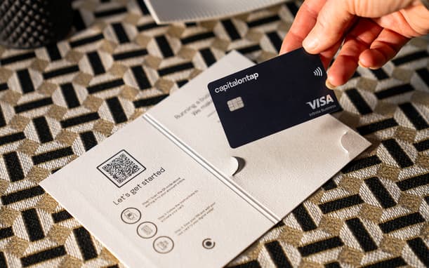Hand Holding A Capital On Tap Visa Card Above Its Welcome Pack Sleeve, Showing Let's Get Started Activation Steps And A QR Code