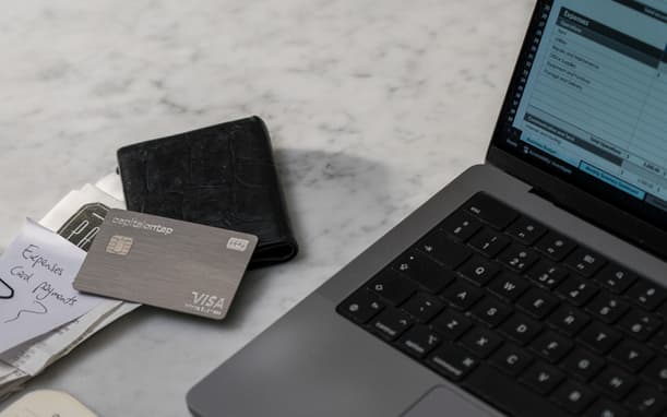 A Capital On Tap Pro Card, Next To A Wallet And Receipts, With A Business Expenses Budget Spreadsheet Open On A Laptop