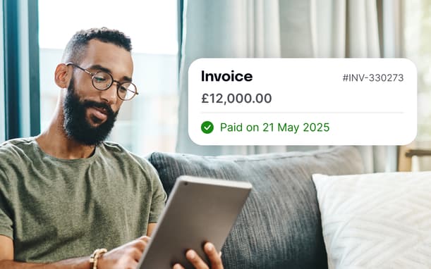 A Man Looking At His Tablet Showing An Invoice For £12,000 Marked As Paid