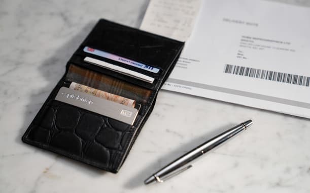 Open Wallet Showing A Capital On Tap Pro Card, UK Driving Licence And Cash, Next To A Delivery Note And Pen On A Marble Surface