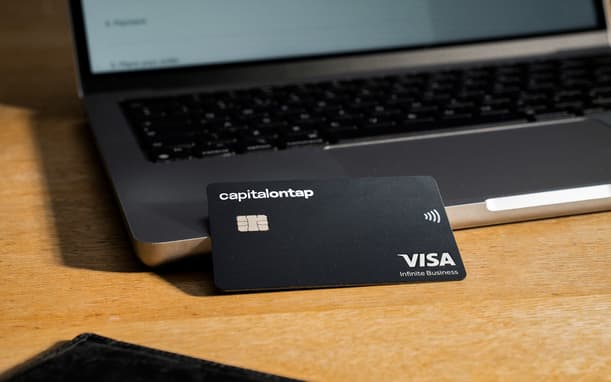 Capital On Tap Visa Infinite Business Card Leaning Against An Open Laptop On A Wooden Desk