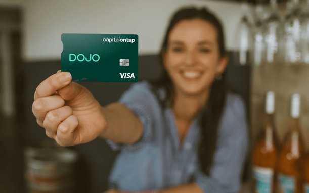 Small Business Owner In Wine Shop Holds Up The Dojo Capital On Tap Business Credit Card Smiling