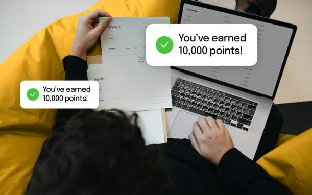 Person Reviewing Paper Invoices Next To A Laptop Showing The Capital On Tap Dashboard, With Notifications Confirming 10,000 Points Earned