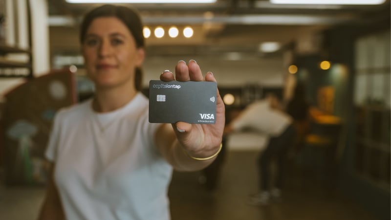 Woman Holding Capital On Tap Card To Camera