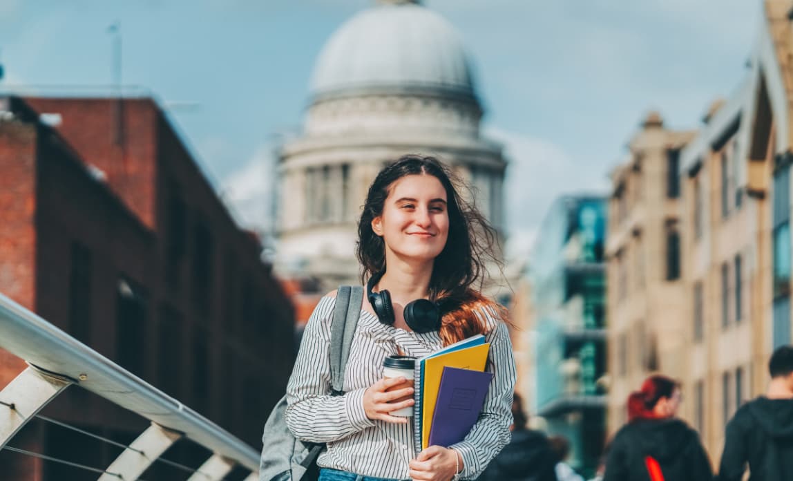 A young woman holding a coffee and books walking and smiling