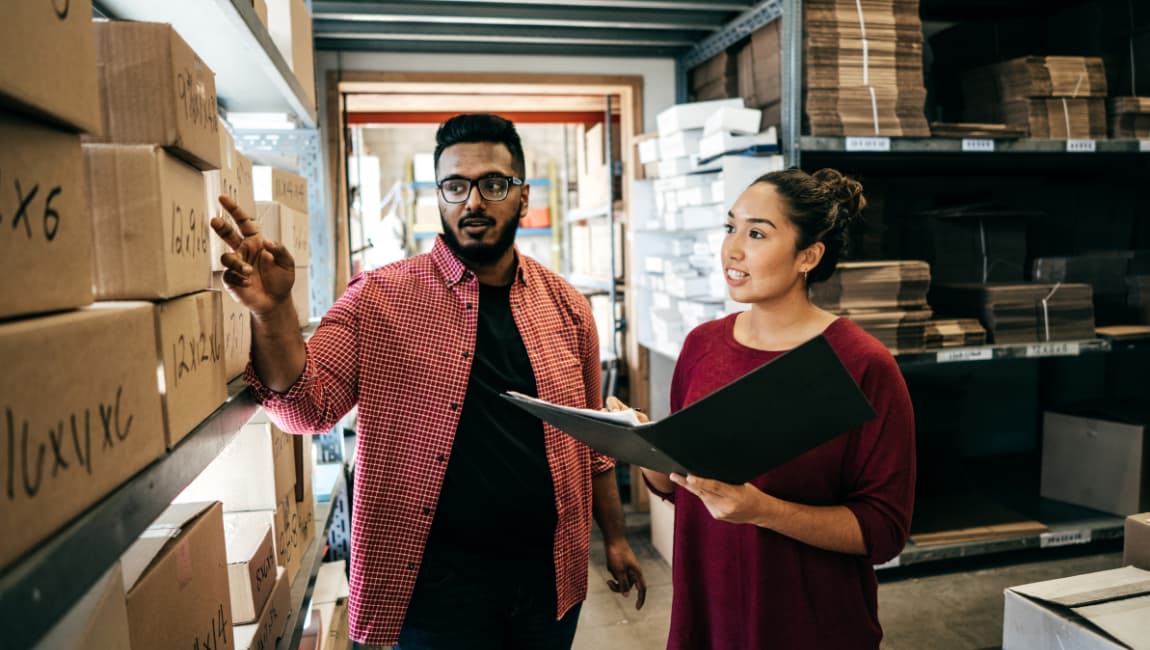 Small Business Partners Performing An Inventory Audit And Stock Take In A Warehouse.