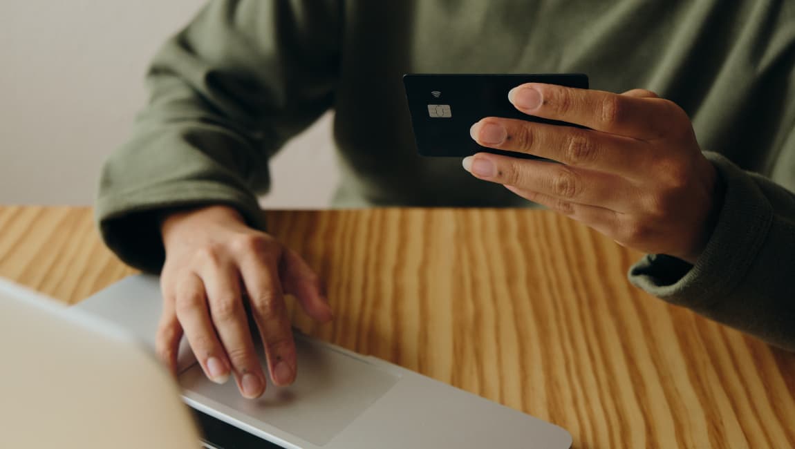 A Close Up Of A Woman's Hands Holding A Black Credit Card Sitting At A Table In Front Of A Laptop