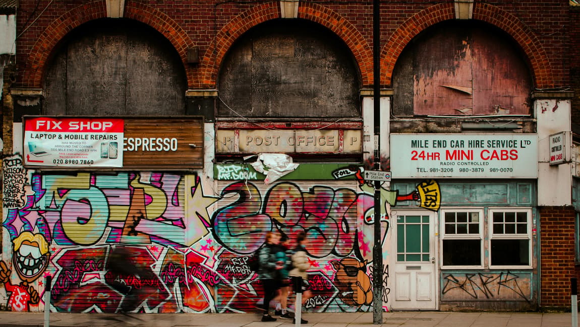 Graffiti Covered Shop Shutters Beneath Boarded Up Arches On A UK High Street