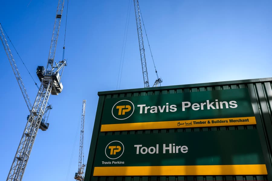 Travis Perkins Timber, Builders Merchant And Tool Hire Signage Against A Blue Sky, With Construction Cranes In The Background