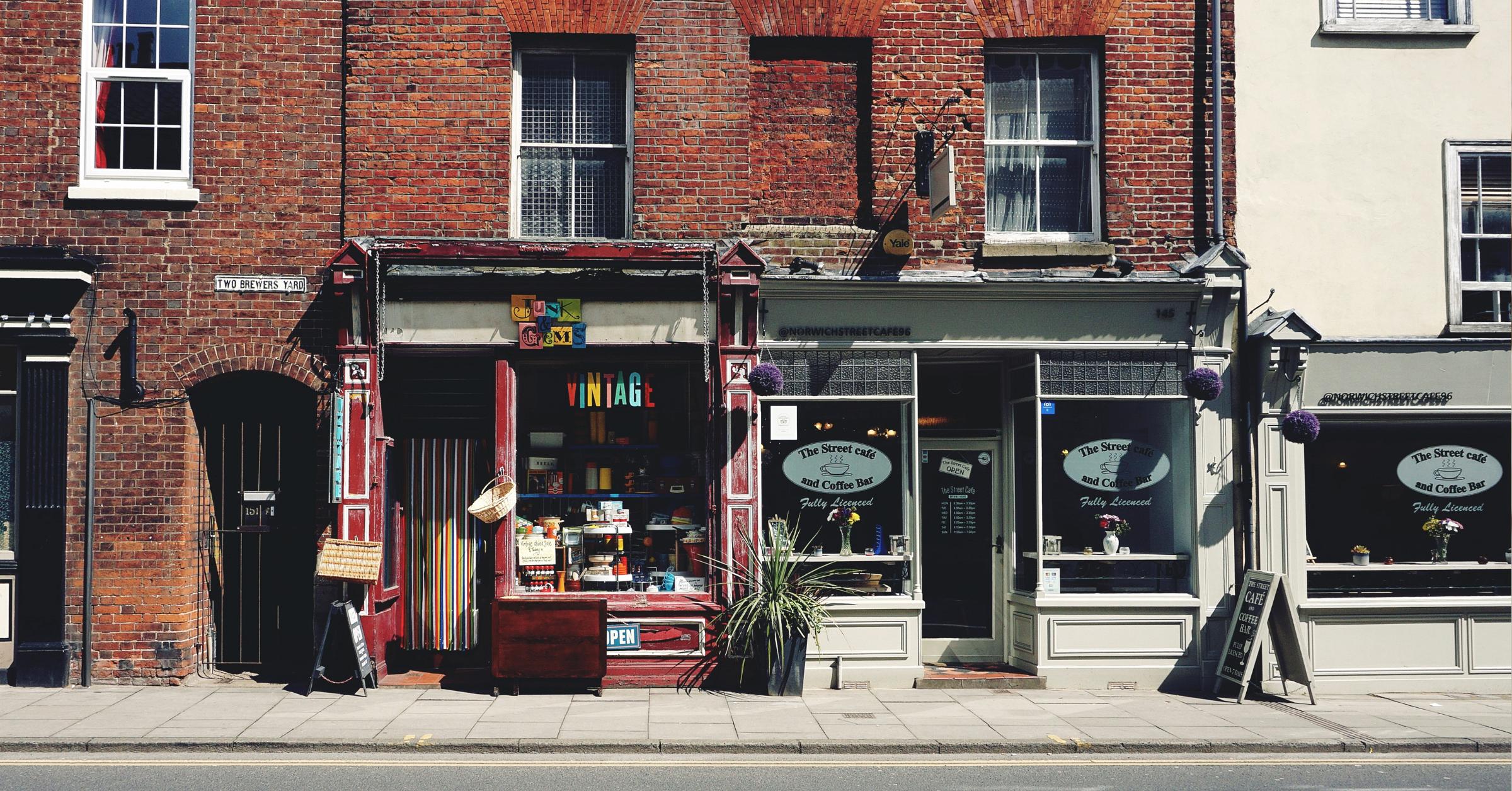 A Red Brick Building With Two Shop Fronts, A Vintage Store And A Cafe.