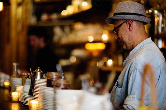 A Small Business Owner Standing Behind The Counter Of A Dimly Lit Cafe