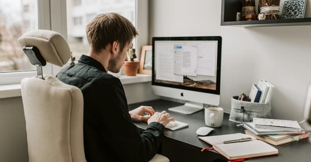 A Man Sitting At His Desk Typing On A Monitor And Keyboard.