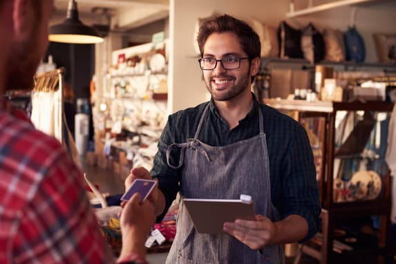 A Shopkeeper In An Apron Accepting A Credit Card Payment