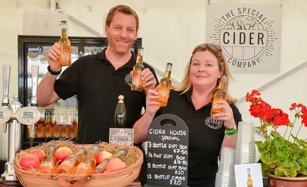 Julia And Mark Hold Up A Cider Bottle Behind A Bar At A Food Festival (1)