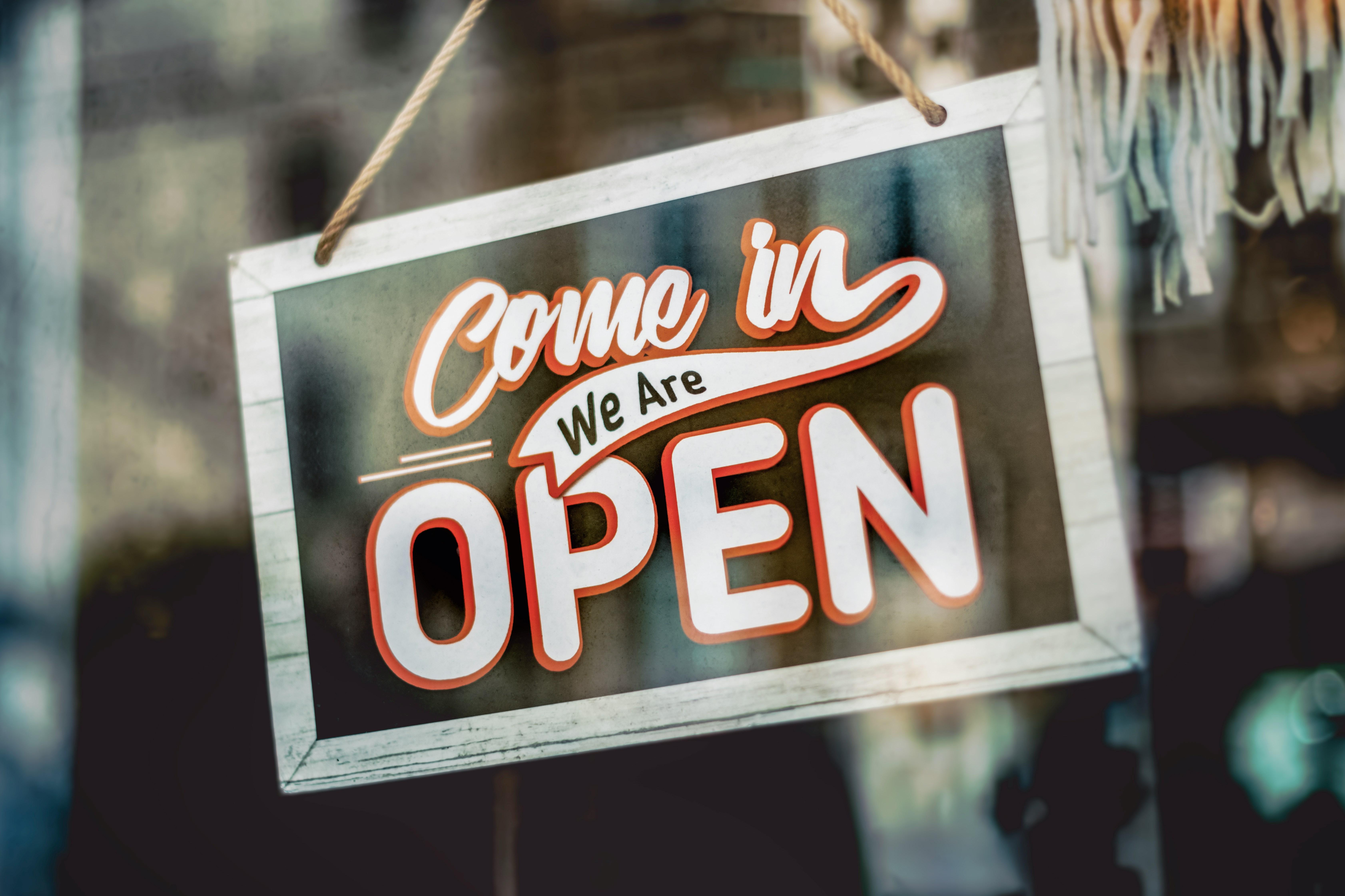 A Brightly Coloured Sign Saying Come In We Are Open Hangining In A Shop Window