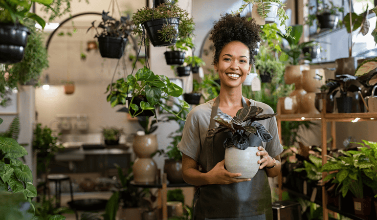 Portrait Of Young Business Owner Smiling And Holding Plant