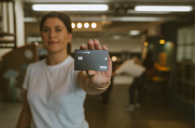 Woman Holding Capital On Tap Card To Camera