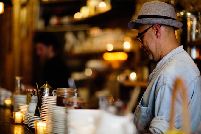A Small Business Owner Standing Behind The Counter Of A Dimly Lit Cafe