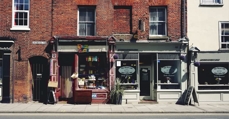 A Red Brick Building With Two Shop Fronts, A Vintage Store And A Cafe.