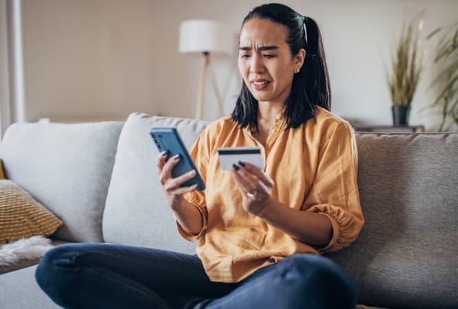 A woman looks confused holding her phone and credit card