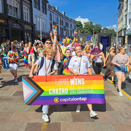 Capital on Tap at Pride Cymru parade holding up a rainbow banner that says love wins