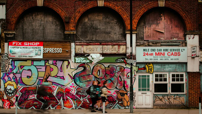Graffiti Covered Shop Shutters Beneath Boarded Up Arches On A UK High Street