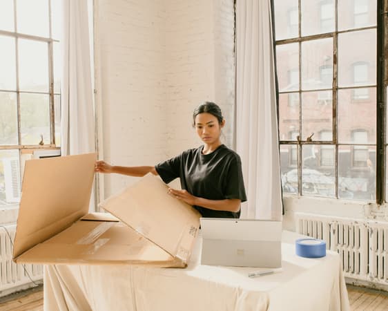 Woman Assembling A Cardboard Shipping Box Next To Her Laptop, Packaging An Order For Her Small Business