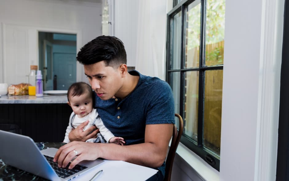 A man types on his laptop holding a baby