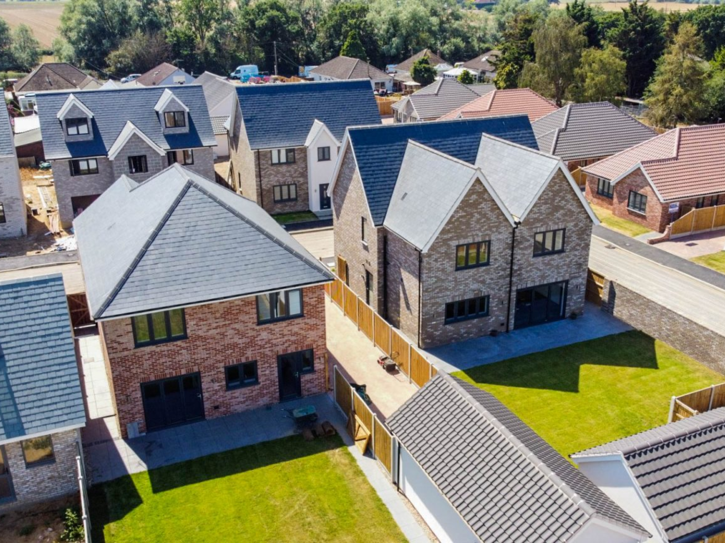 A bird's eye view of houses being built. 4 houses are at the centre of the frame. You can see the front two's back lawn which is illuminated by the sun.